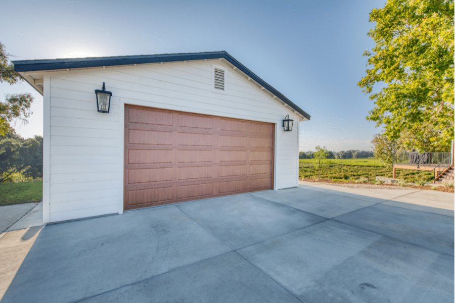 cream one car garage with reddish brown overhead door and black metal roof