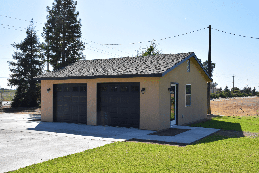 custom tan two car garage with two brown overhead doors and brown roofing