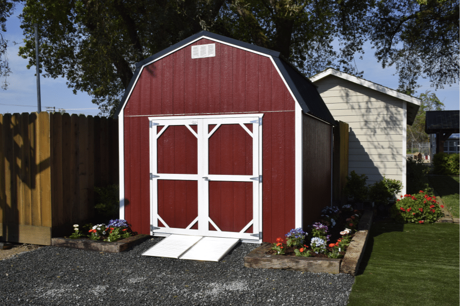 deluxe barn shed that is red and white trimmed with black metal roof ramp and garden bed around it