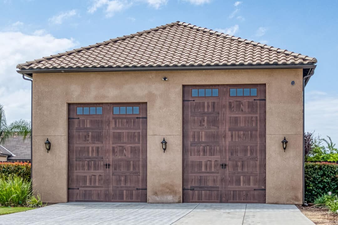 detached two car garage with two brown overhead doors with transom windows each a different size to accomodate different sized vehicles