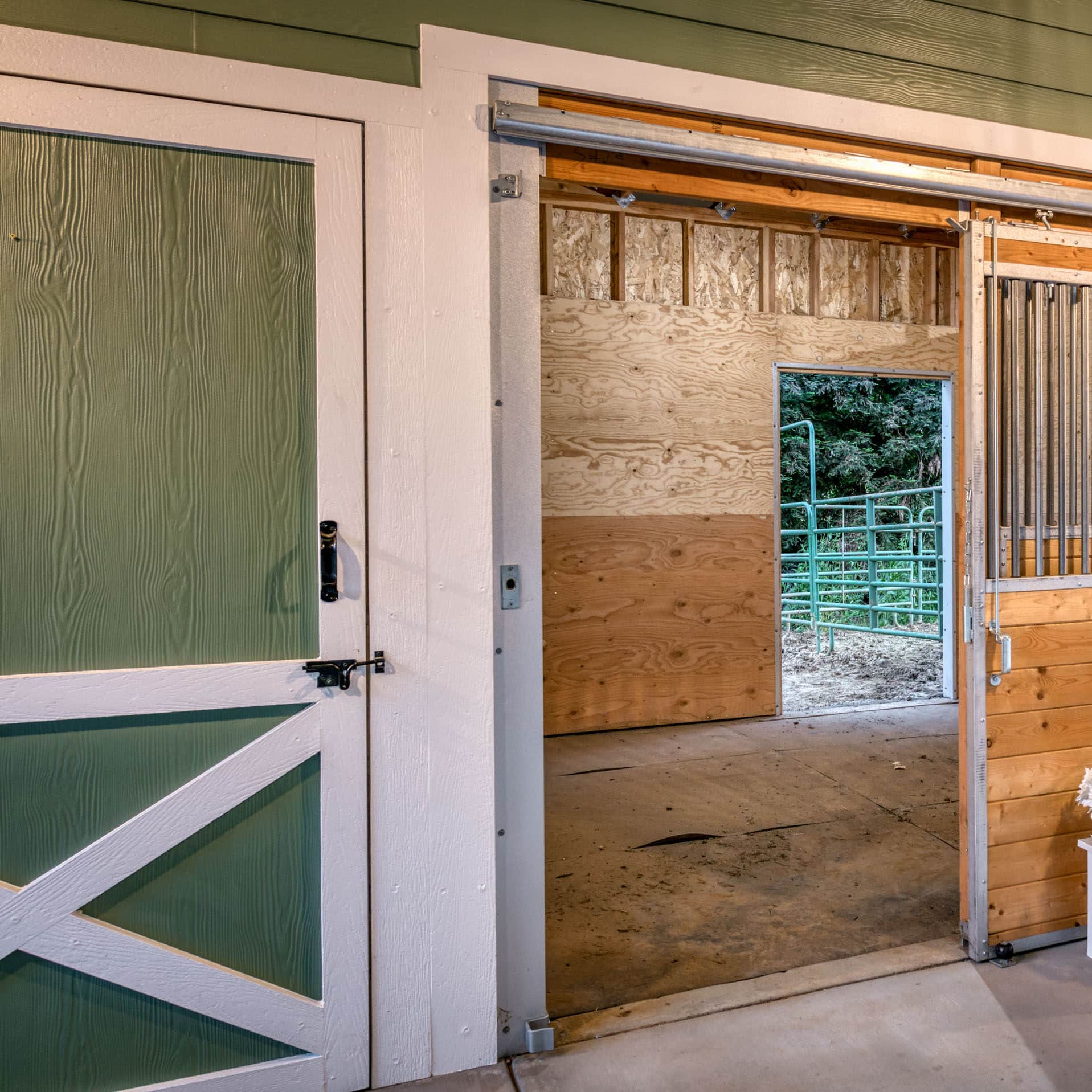 green and white trimmed horse barn with multiple wooden stalls