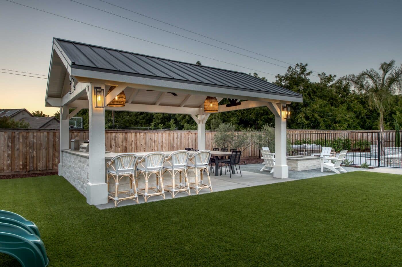grilling set up and kitchen table undeneath white pavilion with black metal roofing beside fire pit and slide