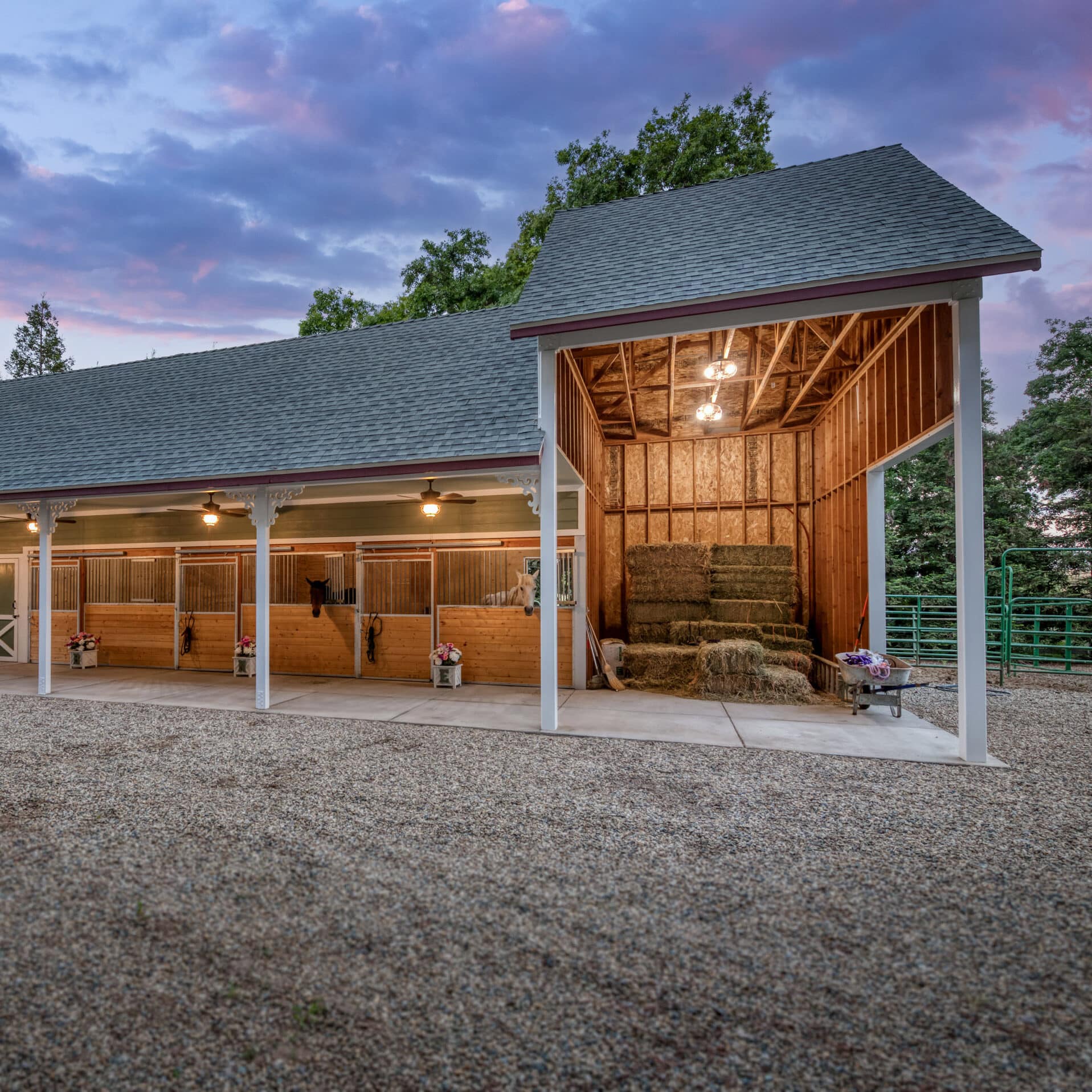 light green horse barn with shingle roof and multiple wooden stalls with hay storage