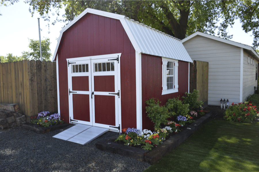 red and white trimmed elite barn shed with white metal roof ramp and garden bed around it