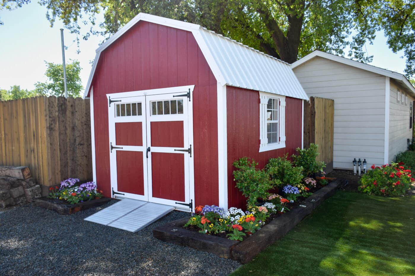 red barn elite shed with white trim and white metal roof featuring ramp leading up to double doors and a garden bed around it