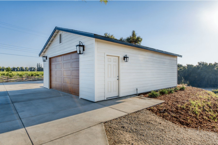 side door on tan 24x30 2-car garage with black metal roofing and a brown overhead garage door