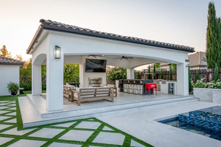side shot of poolside 20x30 cabana with patio, seating area, TV, outdoor kitchen, lighting, and fans