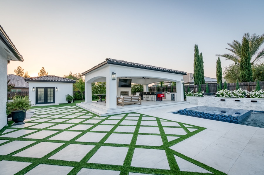 side shot of poolside 20x30 cabana with patio, seating area, TV, outdoor kitchen, lighting, and fans from a distance
