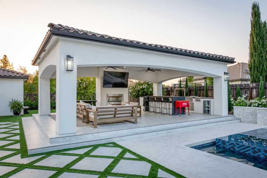 side shot of poolside 20x30 cabana with patio, seating area, TV, outdoor kitchen, lighting, and fans