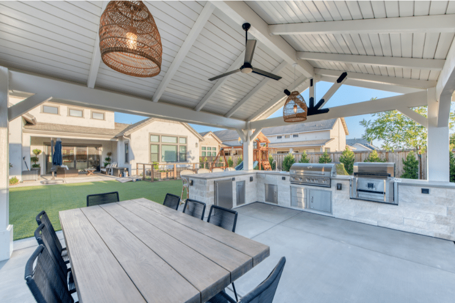 table and outdoor kitchen underneath outdoor pavilion with lights and fans