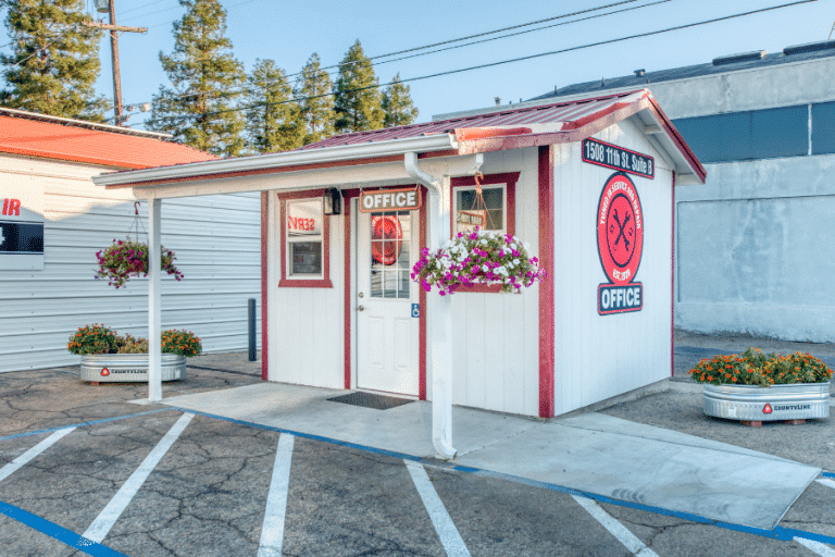 tan and red trimmed custom office shed with porch featuring red metal roofing