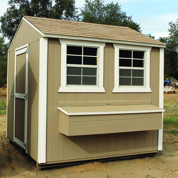 tan and white trimmed chicken coop withe gg collection box below two windows on front