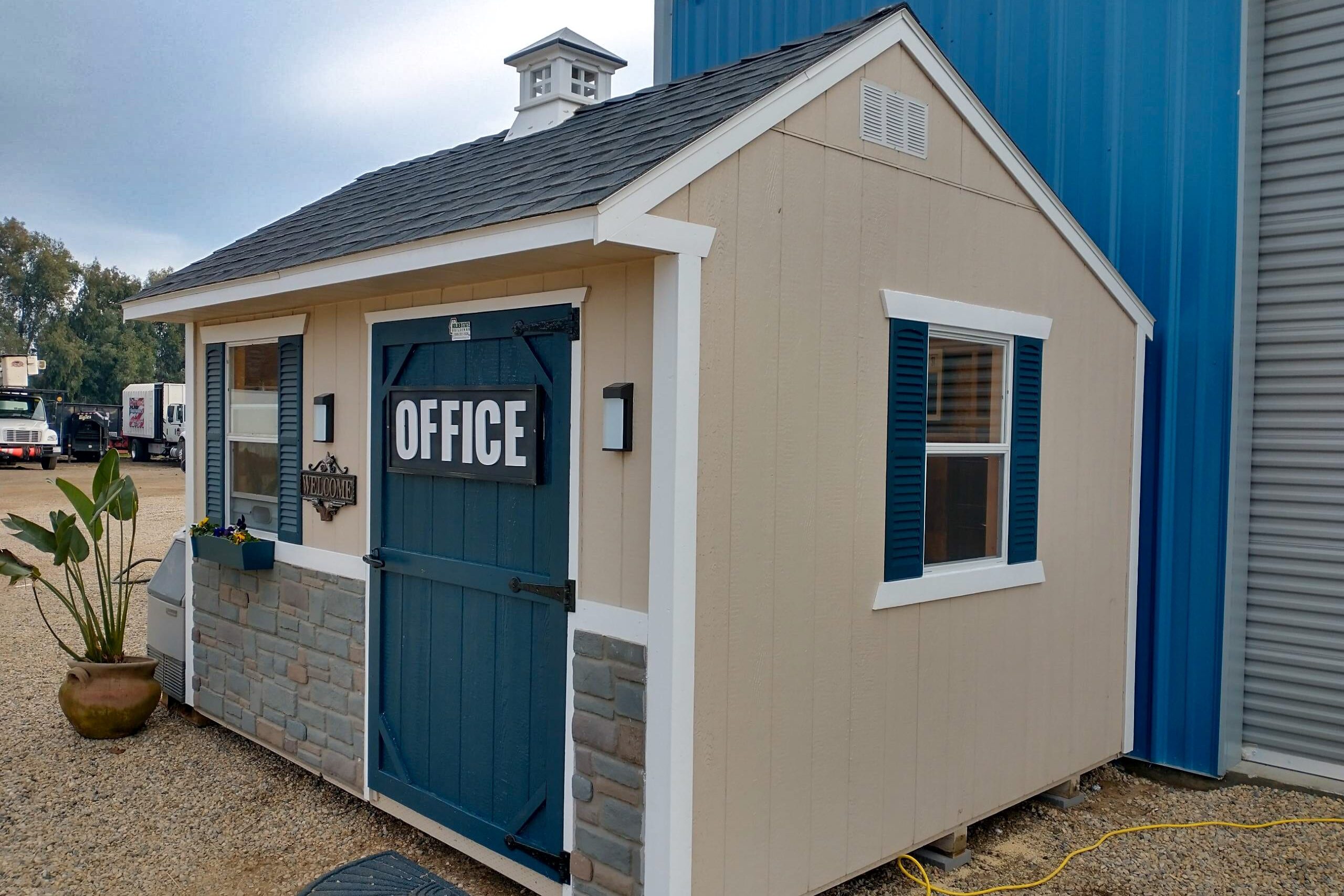 tan and white trimmed office shed with blue front door and gray stone like siding