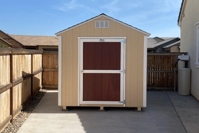 tan and white trimmed value ranch shed with red door along fence on side of home