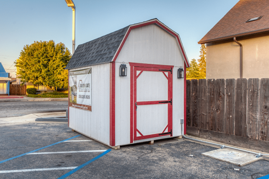 tan barn shed with gray shingle roof and red trim along wooden fence