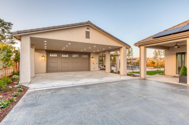 tan garage with darker tan garage door with transom windows and overhang with lighting built in