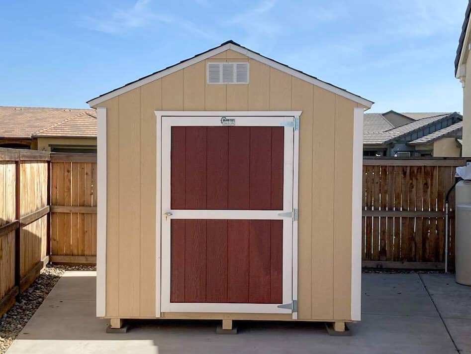 tan rancher sheds near Goshen CA with red door and white trim tucked along side of home and by fence