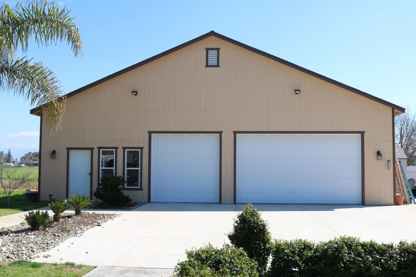 tan three car garage with brown trim and two white overhead doors