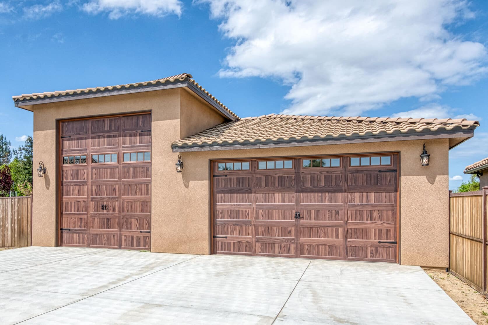 tan three car garage with two different height and lengths of brown garage doors with transom windows