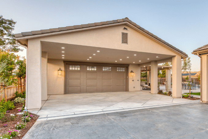 tan two car garage with brown overhead door and overhang on concrete pad