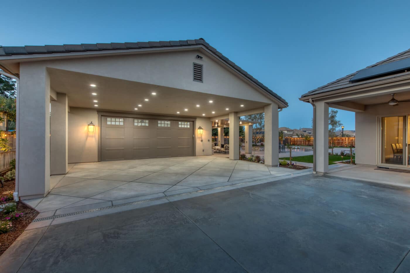 tan two car garage with overhang featuring lighting in it and brown garage door with transom windows