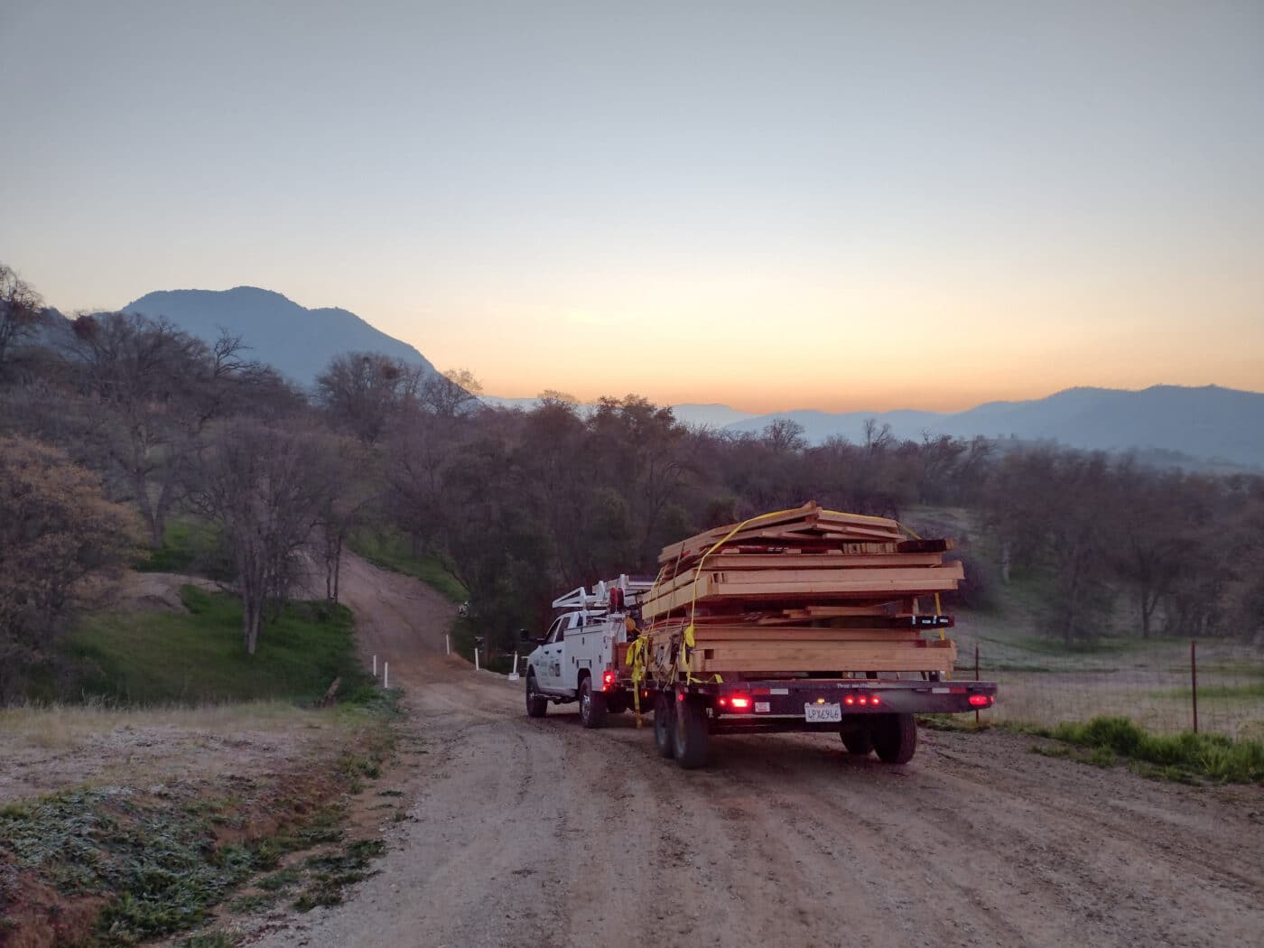 truck driving down gravel road with building on back into sunset