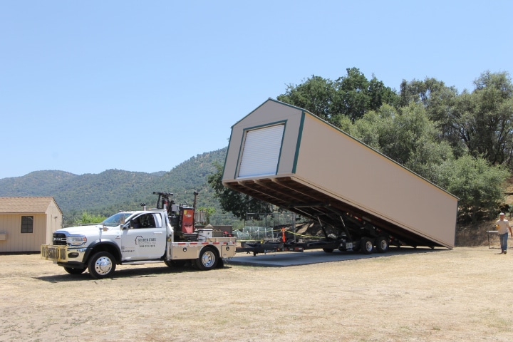 truck tilting trailer bed to drop off tan garage at Shaver Lake property