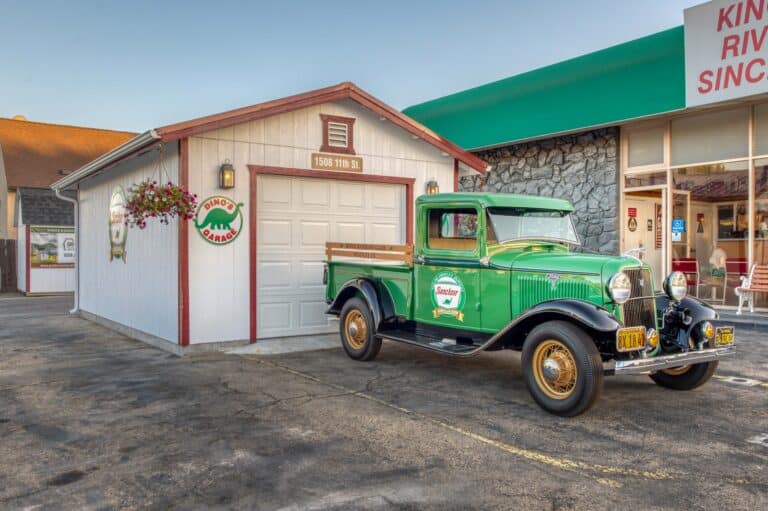 white one car garage with red trim and custom signs and a green old truck in front