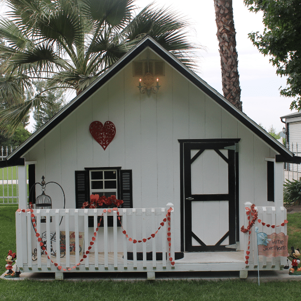 white playhouse with black trim and fron porch decorated with red hearts and flowers