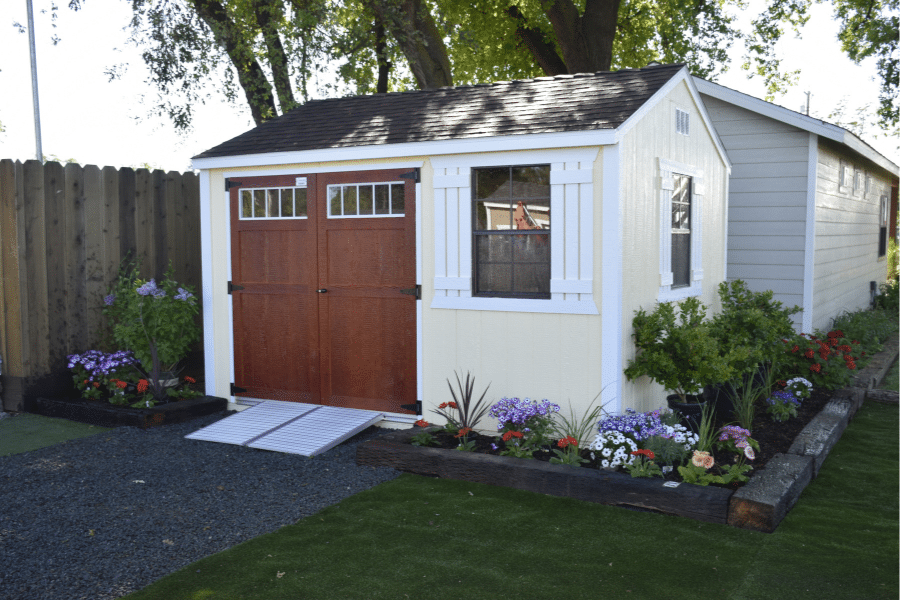 yellow ranch tall shed with brown doors ramp white trim and garden bed around it
